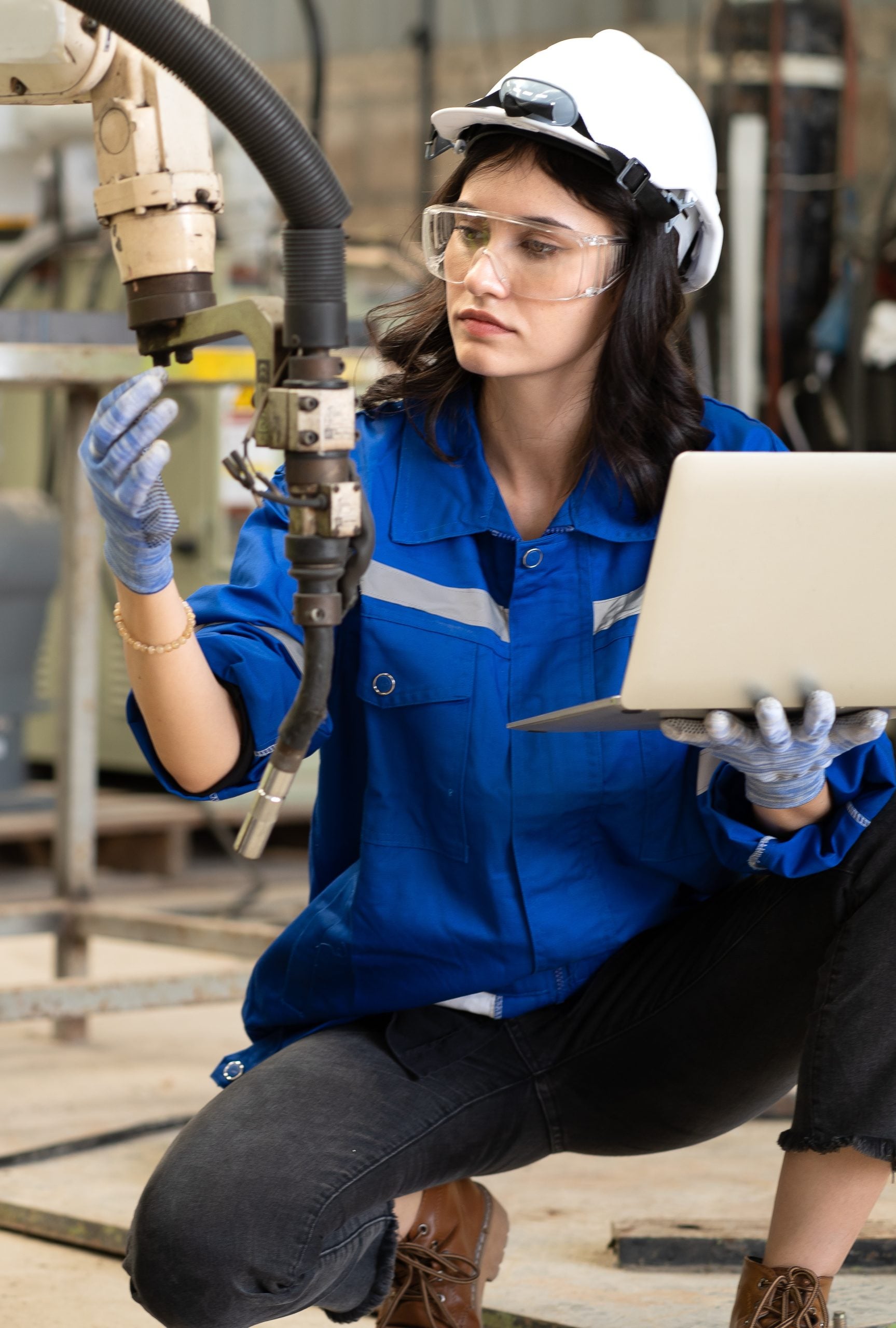 A woman wearing safety goggles and a blue shirt and holding a laptop.